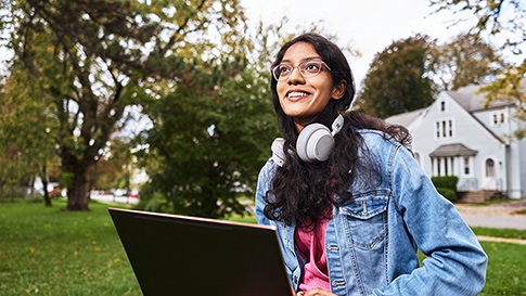 Sabiha sitting outside using her laptop while wearing headphones